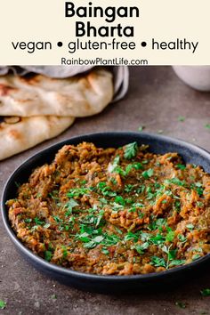 a bowl filled with meat and vegetables on top of a table next to pita bread