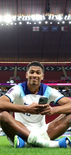 a man sitting on the ground in front of a soccer stadium holding a cell phone