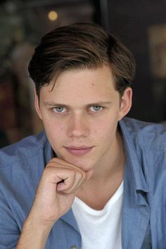 a young man sitting at a table with his hand on his chin looking to the side