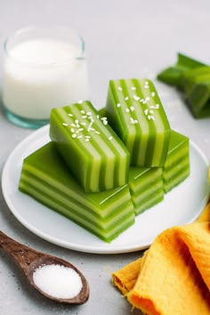 several pieces of green candy on a plate next to a spoon and glass of milk