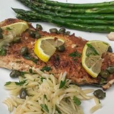 a white plate topped with fish, pasta and asparagus next to lemon wedges