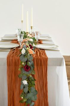 an orange table runner with roses and greenery on it, along with two candles