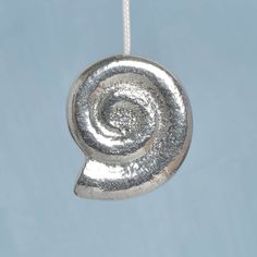 a silver pendant with a spiral design hanging from it's side on a string