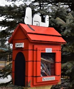 a red mailbox with two cats on top of it in front of some trees