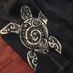 a pair of black jeans with an intricate turtle design on the front and side, sitting on a wooden floor