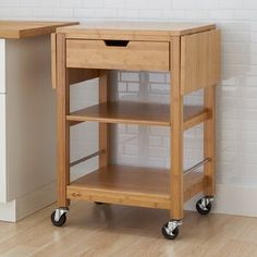 a small wooden table with wheels on the bottom and an open drawer underneath it, in front of a white brick wall