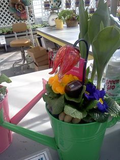 a green watering can filled with flowers and plants