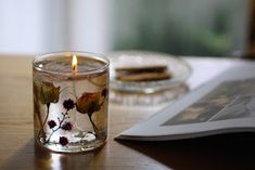 a lit candle sitting on top of a wooden table next to a book and magazine