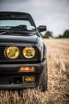 an apple logo on the front of a black car parked in a field with hay