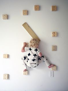 a toddler climbing up the side of a wall with wooden pegs on it