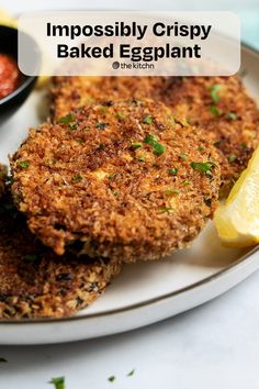 two crab cakes on a plate with lemon wedges and ketchup in the background