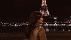 a woman standing in front of the eiffel tower at night with her back turned to the camera