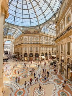 an indoor shopping mall with many people walking around the area and large glass ceilinged ceilings