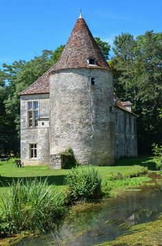 an old stone building with a tower next to a stream in the middle of a field