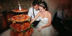 a bride and groom are cutting their wedding cake with two pizzas on the table