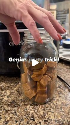 a person reaching into a glass jar filled with brown candies on top of a counter