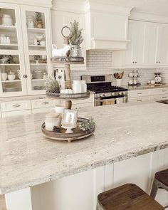 a white kitchen with marble counter tops and wooden stools in front of the island