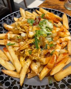 a plate with french fries covered in sauce and toppings on it, sitting on a table