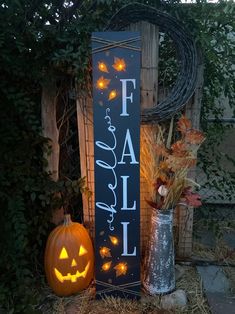 a wooden sign that says fall and two pumpkins in front of it with lights