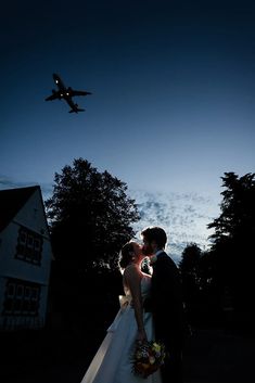 a bride and groom kissing in front of an airplane at night with the moon behind them