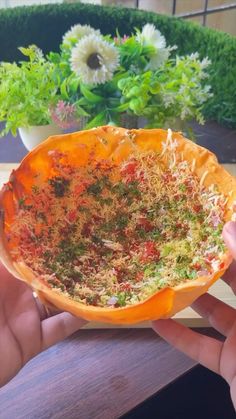 someone is holding up a bowl filled with herbs and other things in front of some potted plants