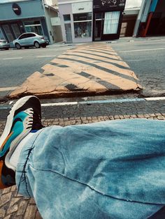 a person's feet resting on the ground in front of a street with buildings