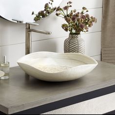 a bowl shaped sink sitting on top of a counter next to a vase with flowers in it