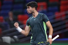 a man holding a tennis racquet in his right hand and wearing a green shirt