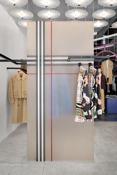 an open closet with clothes hanging from the ceiling and two coats on hangers in front of it