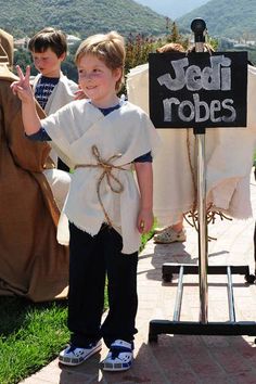 a young boy standing in front of a sign that says jedi robes on it