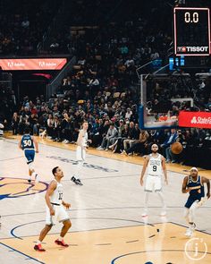 a group of men playing basketball against each other on a court with people watching from the stands