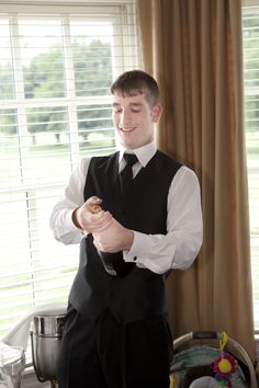 a young man in a vest and tie is holding a piece of bread while standing next to a window