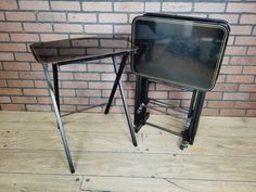 two black tables sitting next to each other on top of a wooden floor near a brick wall