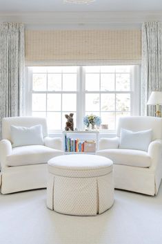 a living room with two white chairs and a coffee table in front of a window