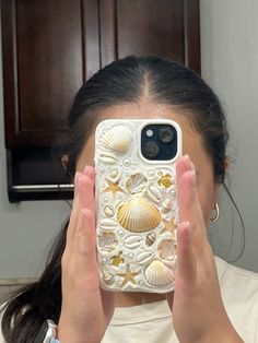 a woman is holding up her phone to take a selfie with seashells on it