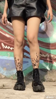 a woman with tattoos on her legs standing in front of a wall