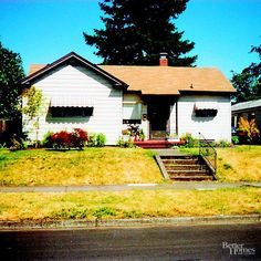 a white house sitting on the side of a road next to a lush green field