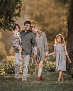 a man and two girls are holding hands as they walk through the grass in front of trees