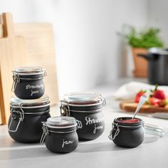 four black jars with labels on them sitting on a counter next to some strawberries