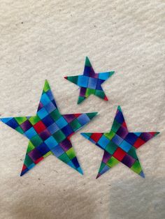 three colorful paper stars sitting on top of a piece of white paper next to each other