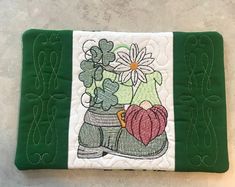 a quilted pot holder with flowers and boots on the front, sitting on a tile floor