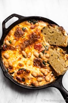 a skillet filled with bread and beans on top of a white countertop next to a piece of bread