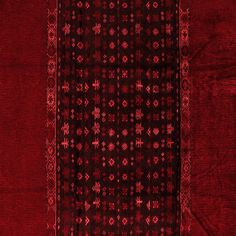 a red and black area rug with an intricate design on the bottom, in front of a dark background