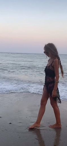 a woman walking on the beach at sunset