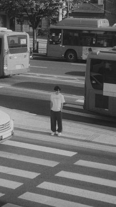 a man standing in the middle of a crosswalk with buses and cars behind him