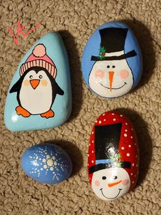 three painted rocks with snowman, penguin and penguin in hats on the ground next to each other