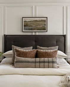 a bed with pillows and blankets on top of it next to a framed painting above the headboard