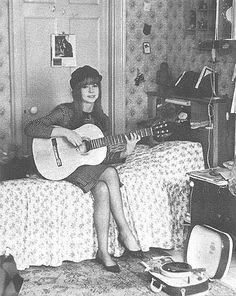 a woman is sitting on her bed playing the guitar