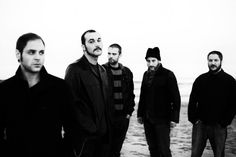 five men standing on the beach in black and white