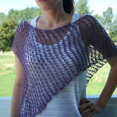 a woman standing in front of a window with her hands on her hips wearing a purple knitted shawl